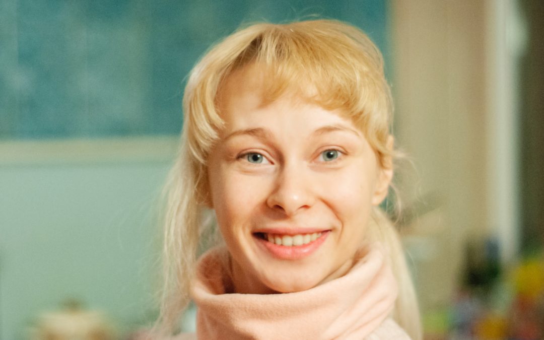 Girl with blonde hair and blue eyes in a pink turtle neck smiling at the camera
