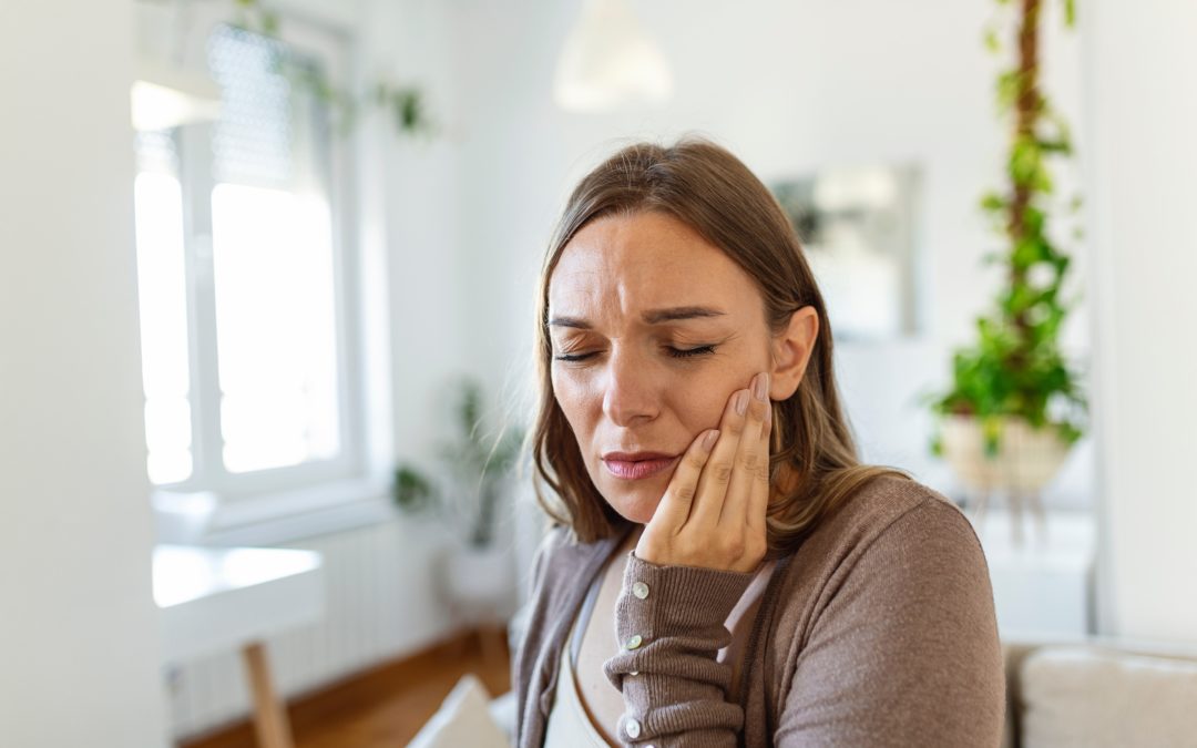 Girl in grey shirt holding jaw in pain.